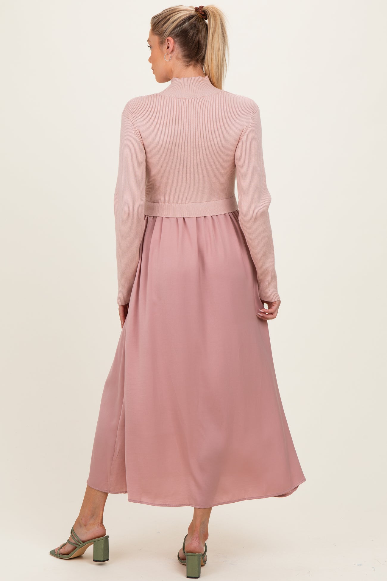 woman wearing a pink maternity dress with a ribbed top and flowing skirt, showing her back and styled with green heels