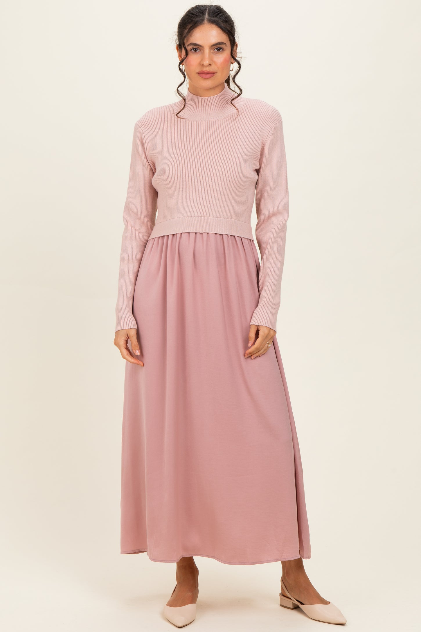 woman wearing a light pink long sleeve ribbed maxi dress with a fitted bodice and flowy skirt, standing against a neutral background