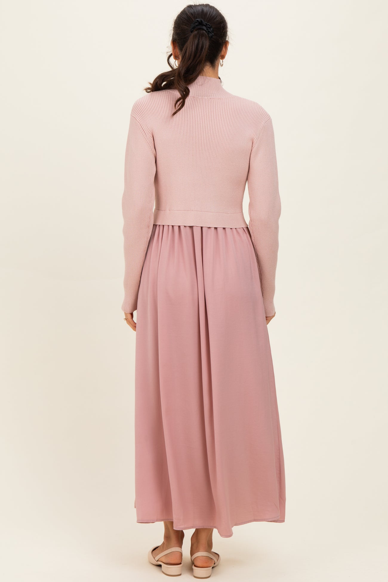 woman wearing a light pink ribbed sweater top with a flowy pink maxi skirt from the back
