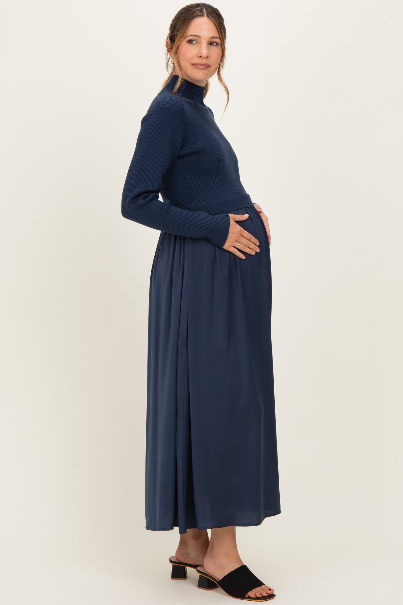 woman wearing a navy blue maternity maxi dress with a ribbed long sleeve top and a flowing skirt, gently cradling her baby bump