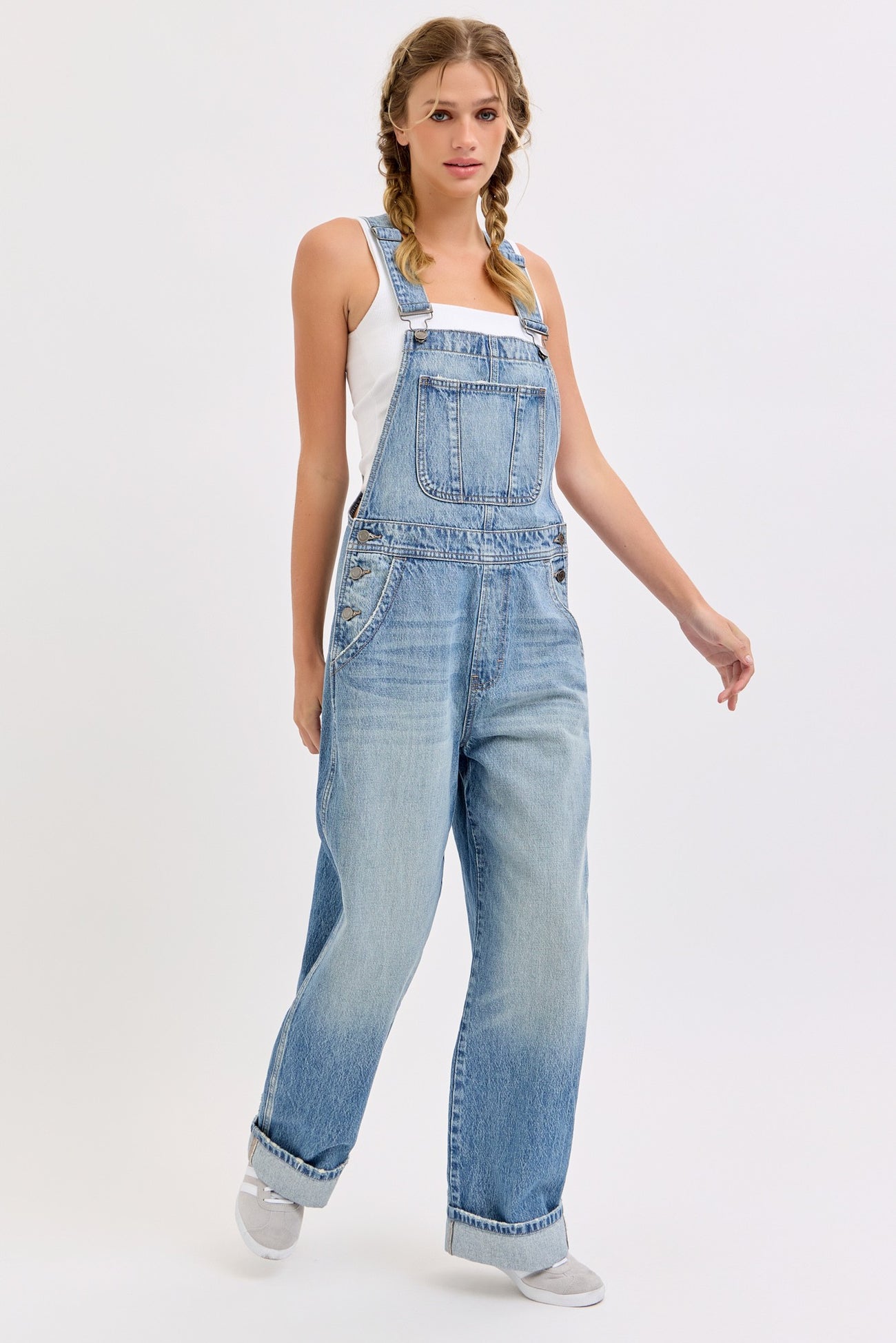 woman wearing light blue oversized denim overalls with a white tank top underneath and braids in her hair