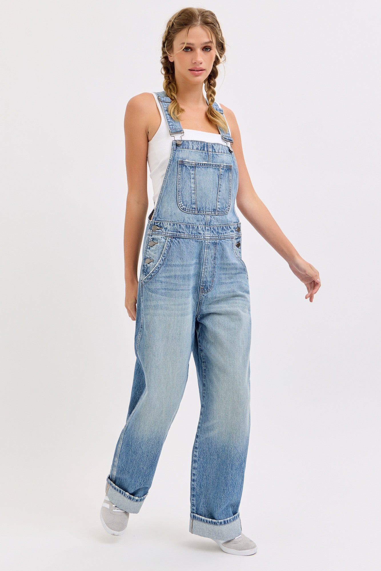 woman wearing light blue oversized denim overalls with a white tank top underneath and braids in her hair