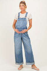 woman wearing a light blue maternity overall with a white shirt and holding her baby bump