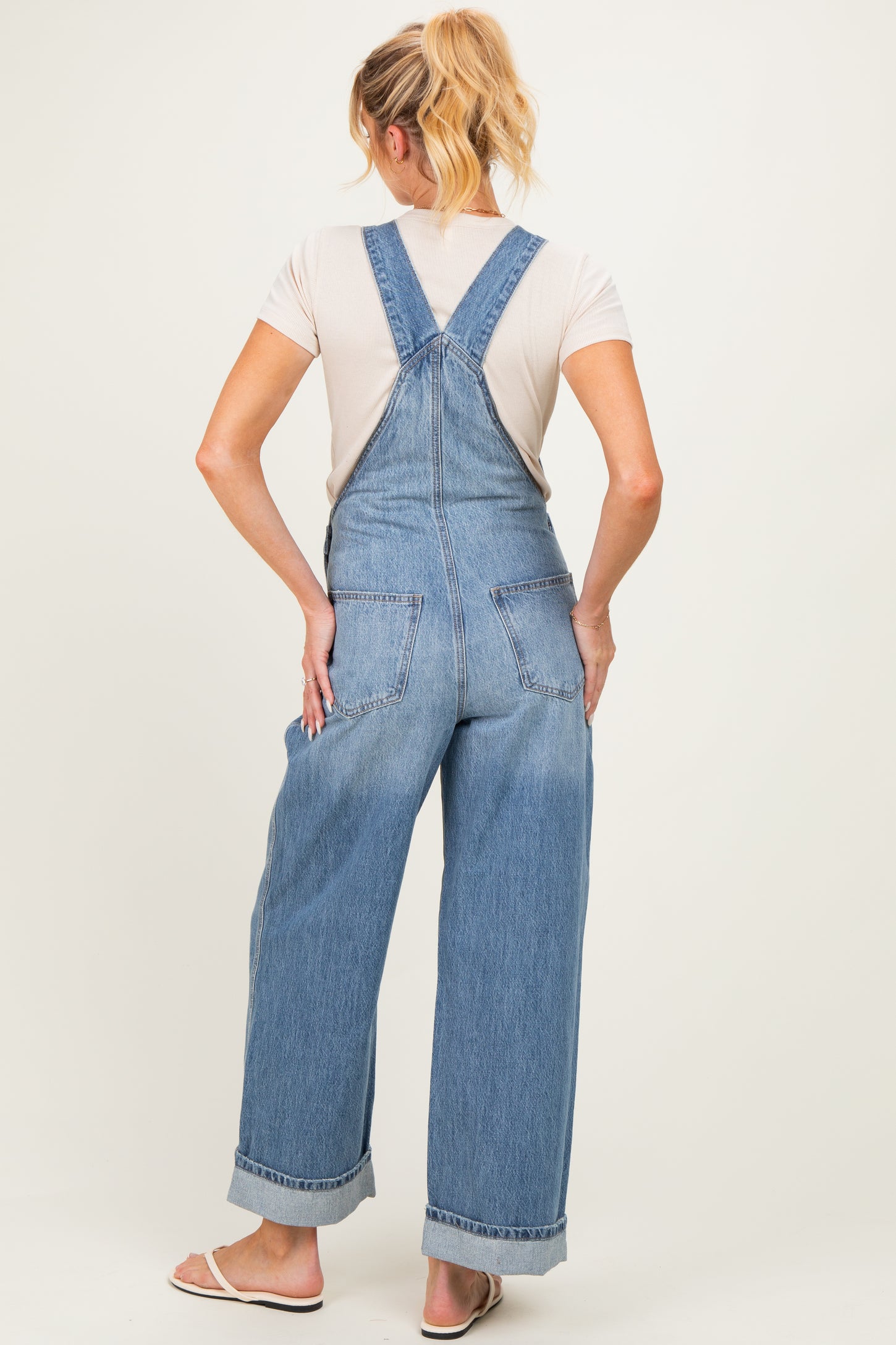 woman wearing light blue denim maternity overalls with a relaxed fit and rolled cuffs, showing the back view