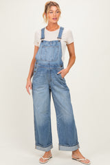 woman wearing a light blue maternity denim overalls with a white t-shirt underneath and standing casually