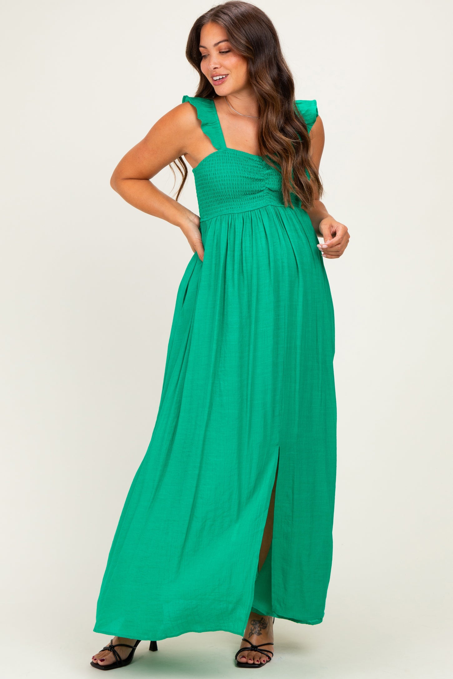 woman wearing a vibrant green maternity maxi dress with ruffled straps and a front slit, showing her baby bump