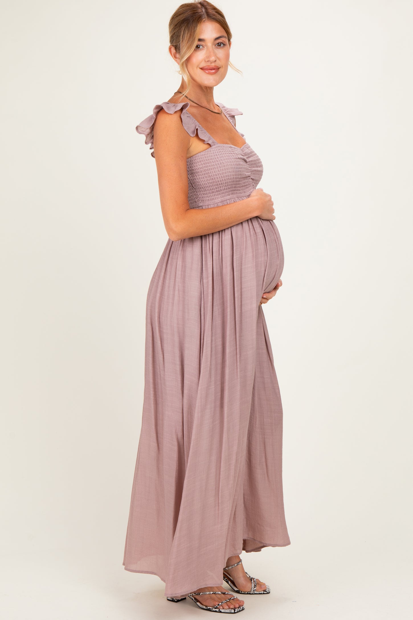 woman wearing a mauve maternity maxi dress with ruffled straps and holding her baby bump