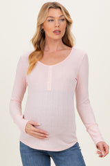 woman wearing a light pink maternity long sleeve top with button details and a visible baby bump