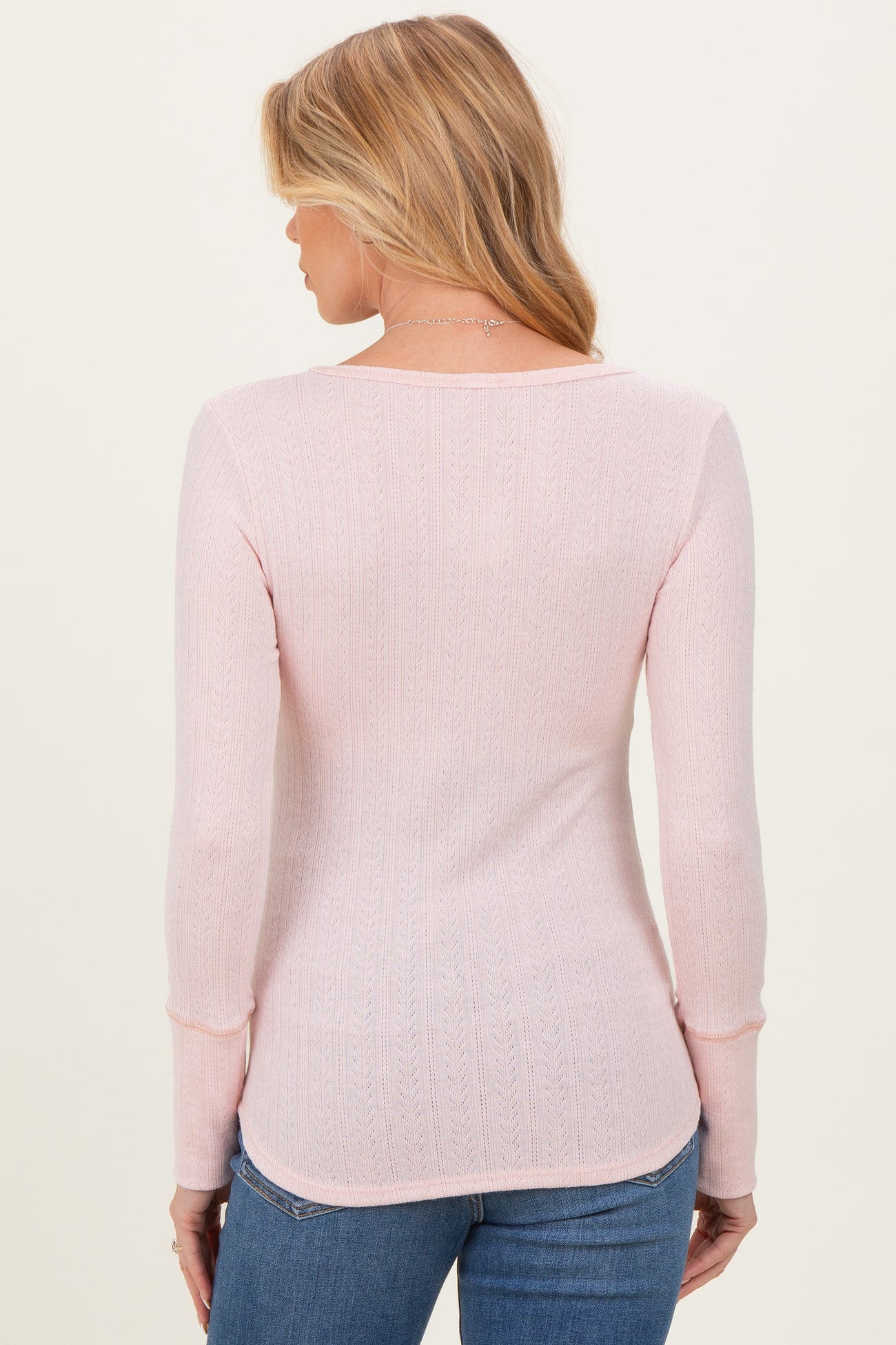 woman wearing a light pink long sleeve maternity top with a ribbed texture, seen from the back