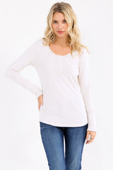 woman wearing a light beige long sleeve henley top with button details and paired with blue jeans