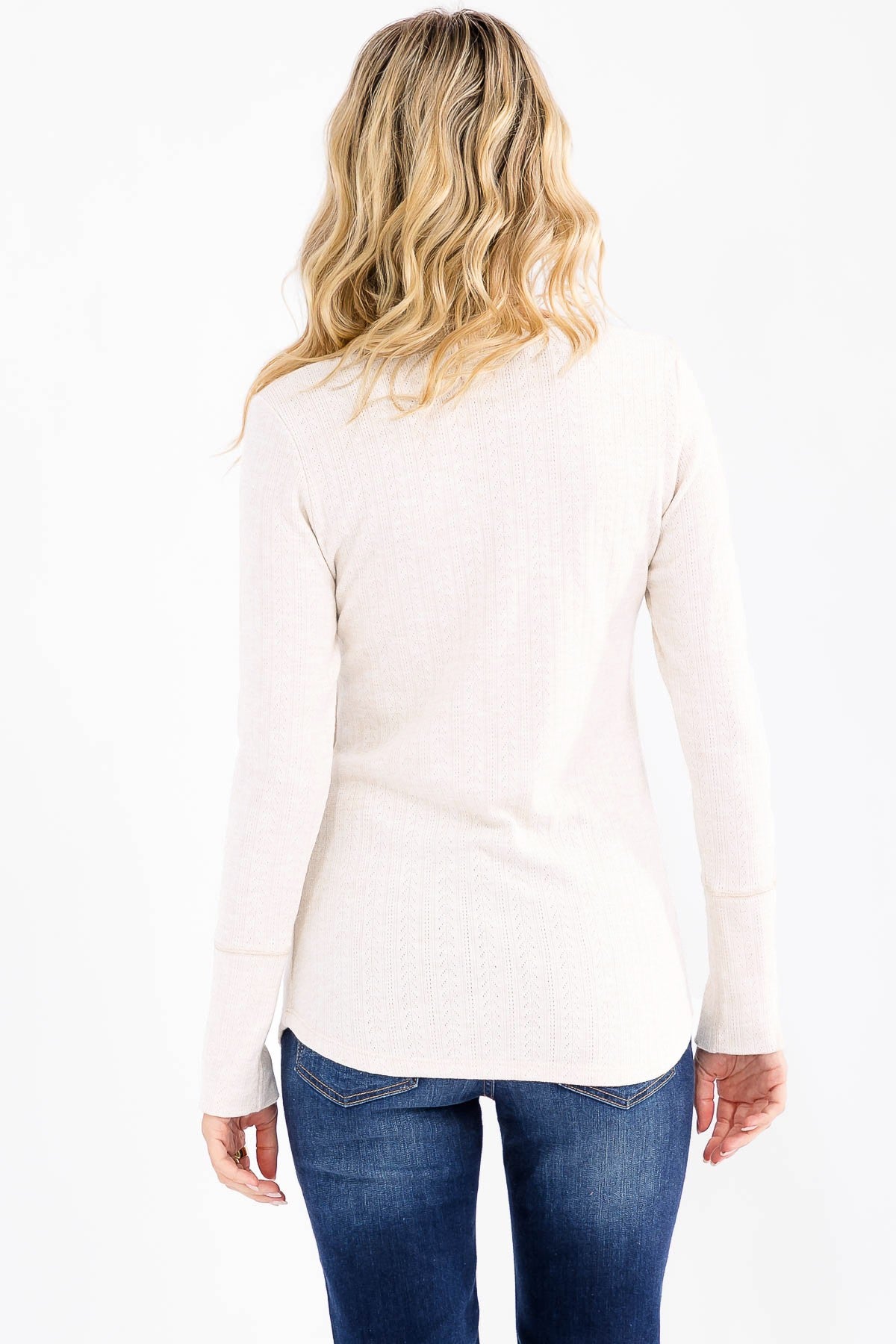 woman wearing a light beige long sleeve top with a ribbed texture and rounded hem paired with dark blue jeans