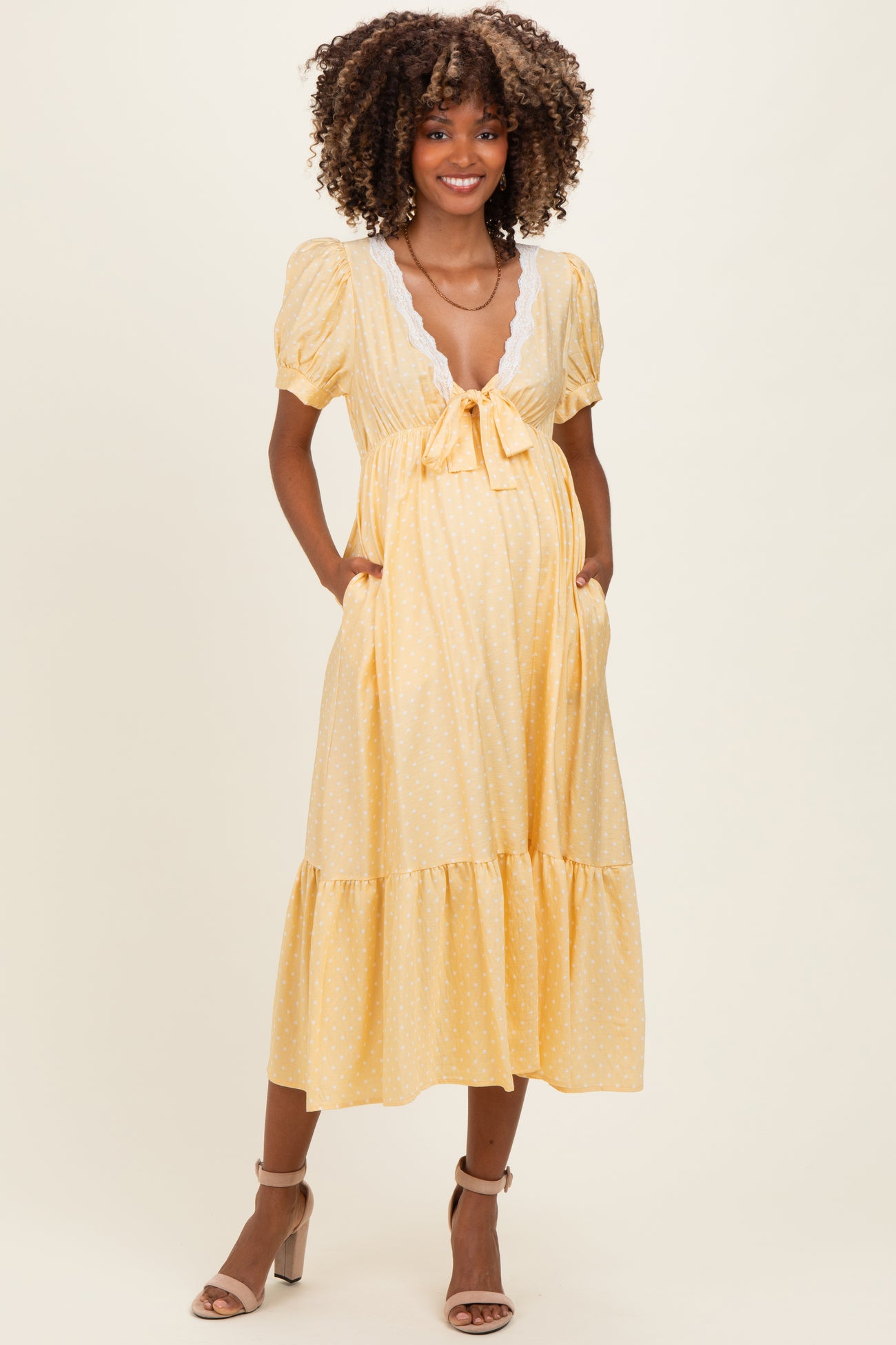 woman wearing a yellow polka dot maternity dress with short puff sleeves, a tie front, and pockets