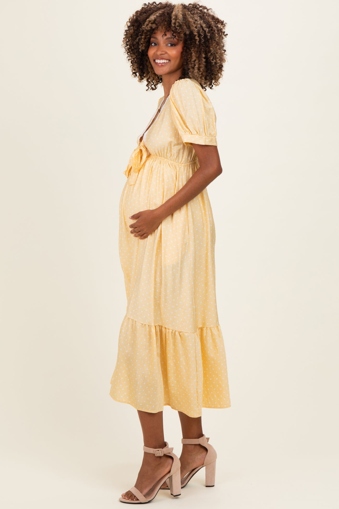 woman wearing a yellow polka dot maternity dress with puff sleeves and a tiered hem, holding her baby bump