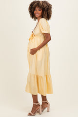 woman wearing a yellow polka dot maternity dress with puff sleeves and a tiered hem, holding her baby bump