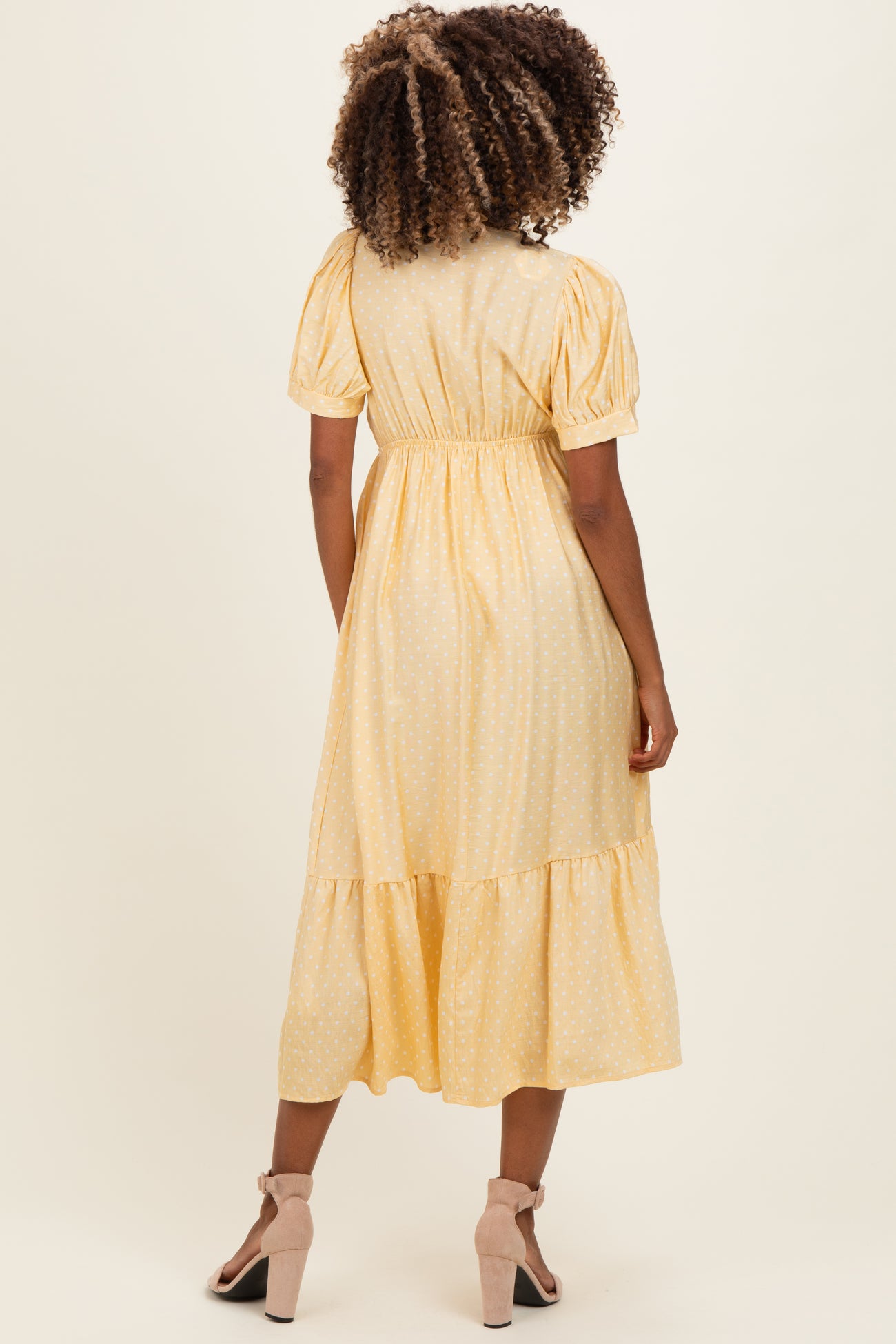 woman wearing a yellow polka dot maternity dress with puff sleeves and a tiered hem, viewed from the back