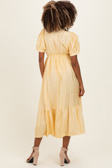 woman wearing a yellow polka dot maternity dress with puff sleeves and a tiered hem, viewed from the back