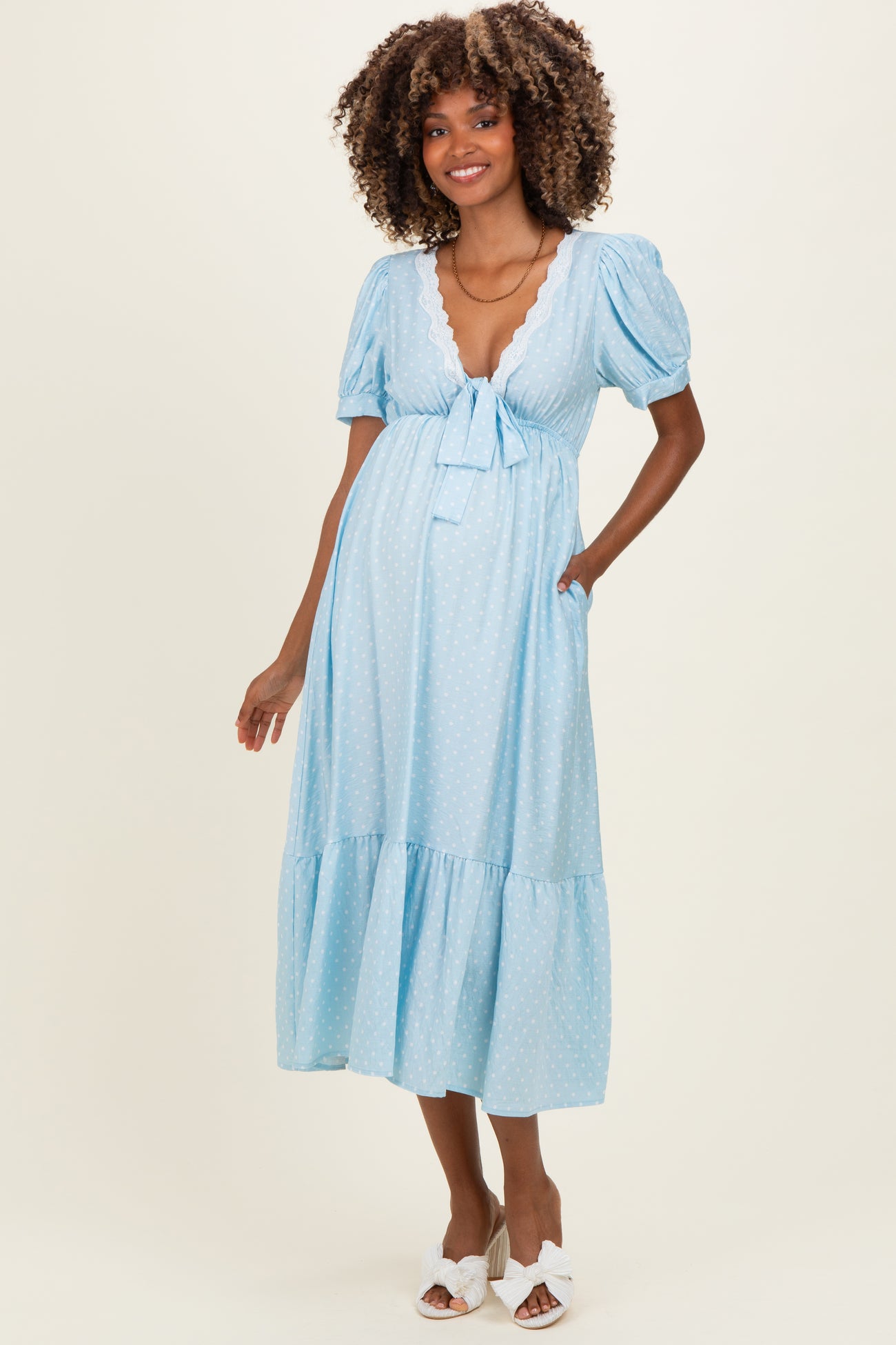woman wearing a light blue maternity dress with puff sleeves, a tie front, and a tiered skirt