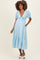 woman wearing a light blue maternity dress with puff sleeves, a tie front, and a tiered skirt