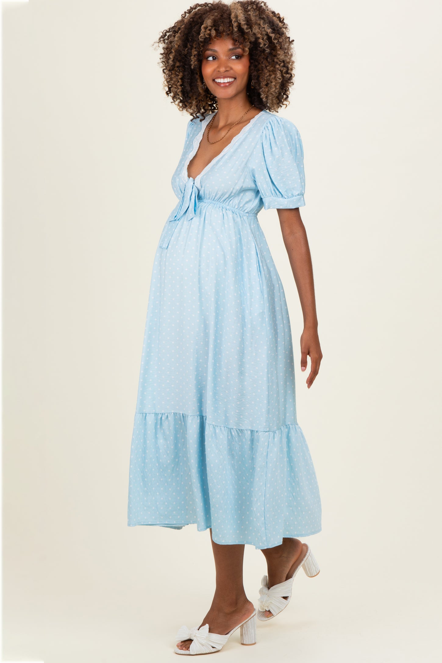 woman wearing a light blue polka dot maternity dress with a tie waist and puff sleeves, showing her baby bump