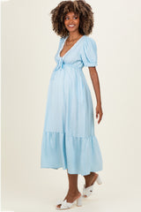 woman wearing a light blue polka dot maternity dress with a tie waist and puff sleeves, showing her baby bump