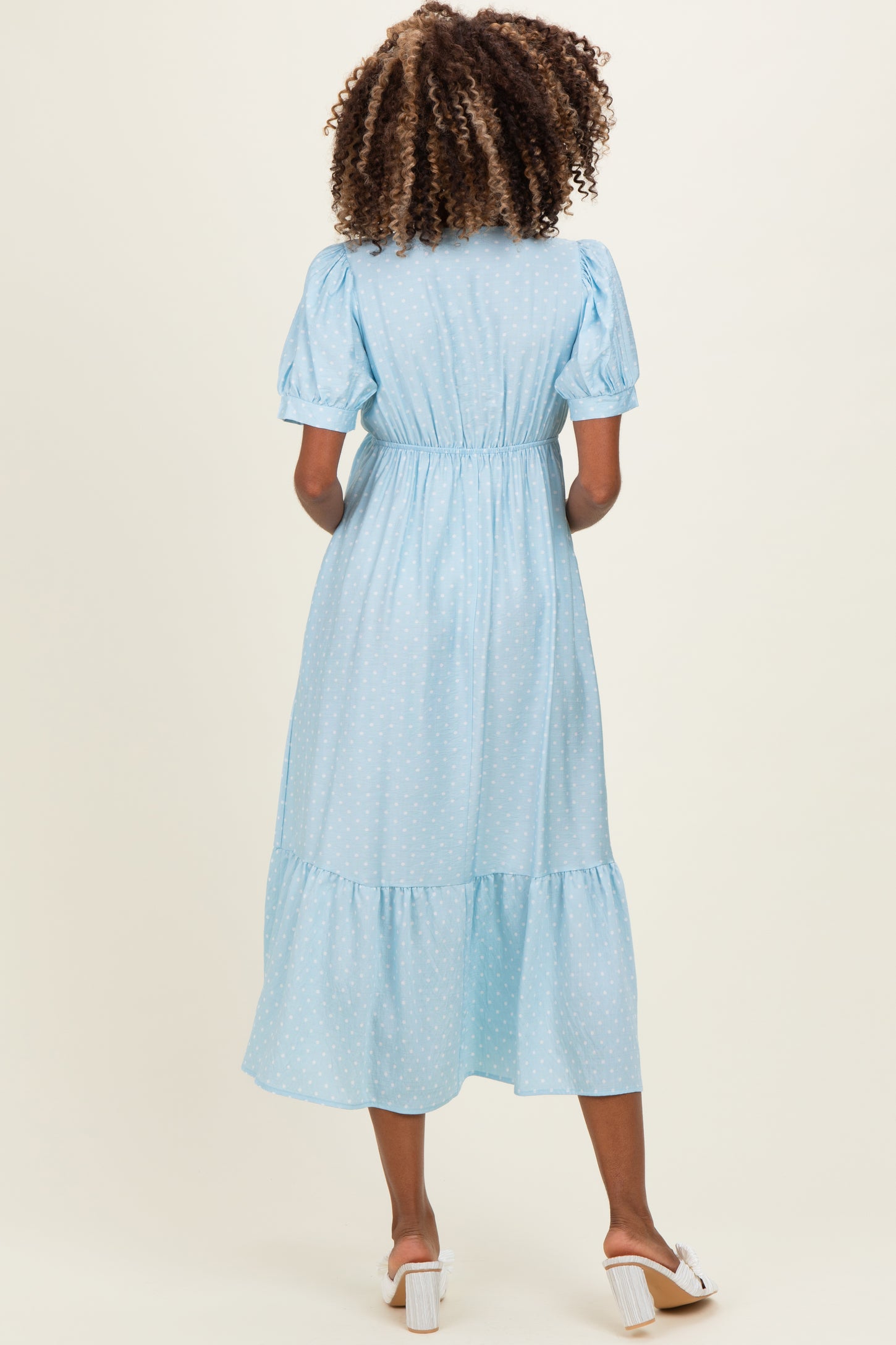 woman wearing a light blue polka dot maternity dress with puff sleeves and a tiered skirt, showing her baby bump