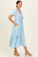 woman wearing a light blue dotted midi dress with short puff sleeves and a tie front, featuring side pockets and a tiered hem