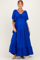 woman wearing a bright blue maternity maxi dress with flutter sleeves and a tie detail at the front, showing her baby bump