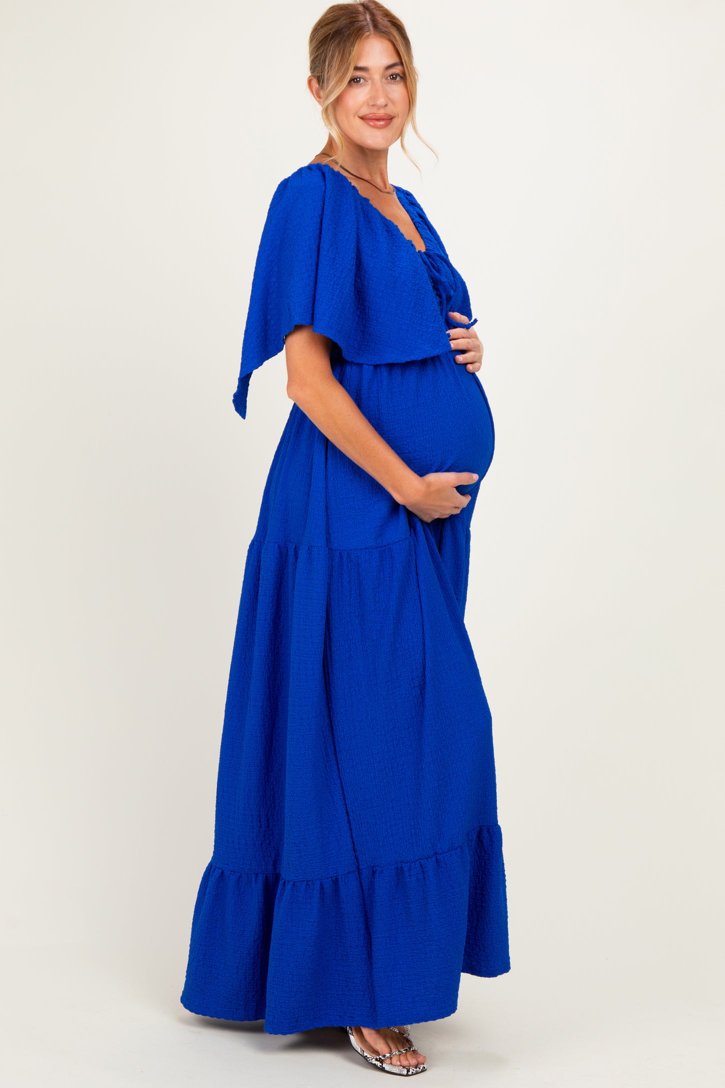 woman wearing a bright blue maternity maxi dress with ruffled sleeves and a visible baby bump