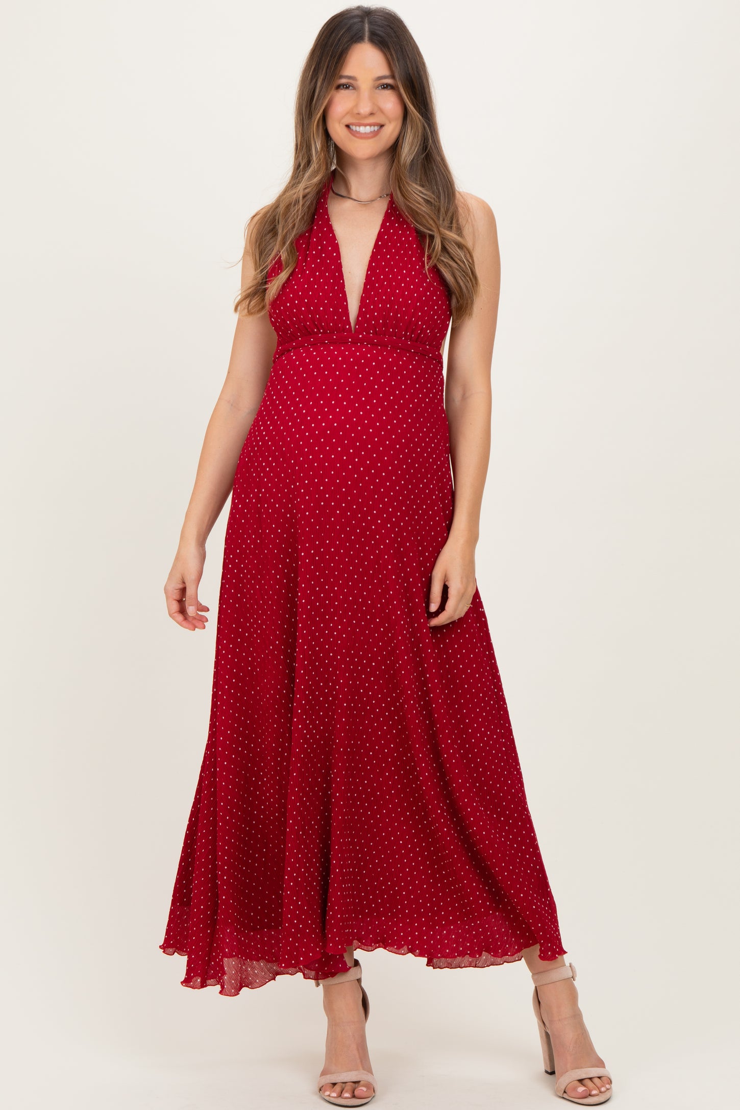 woman wearing a red polka dot maternity dress with a halter neckline and flowing skirt, showcasing her baby bump