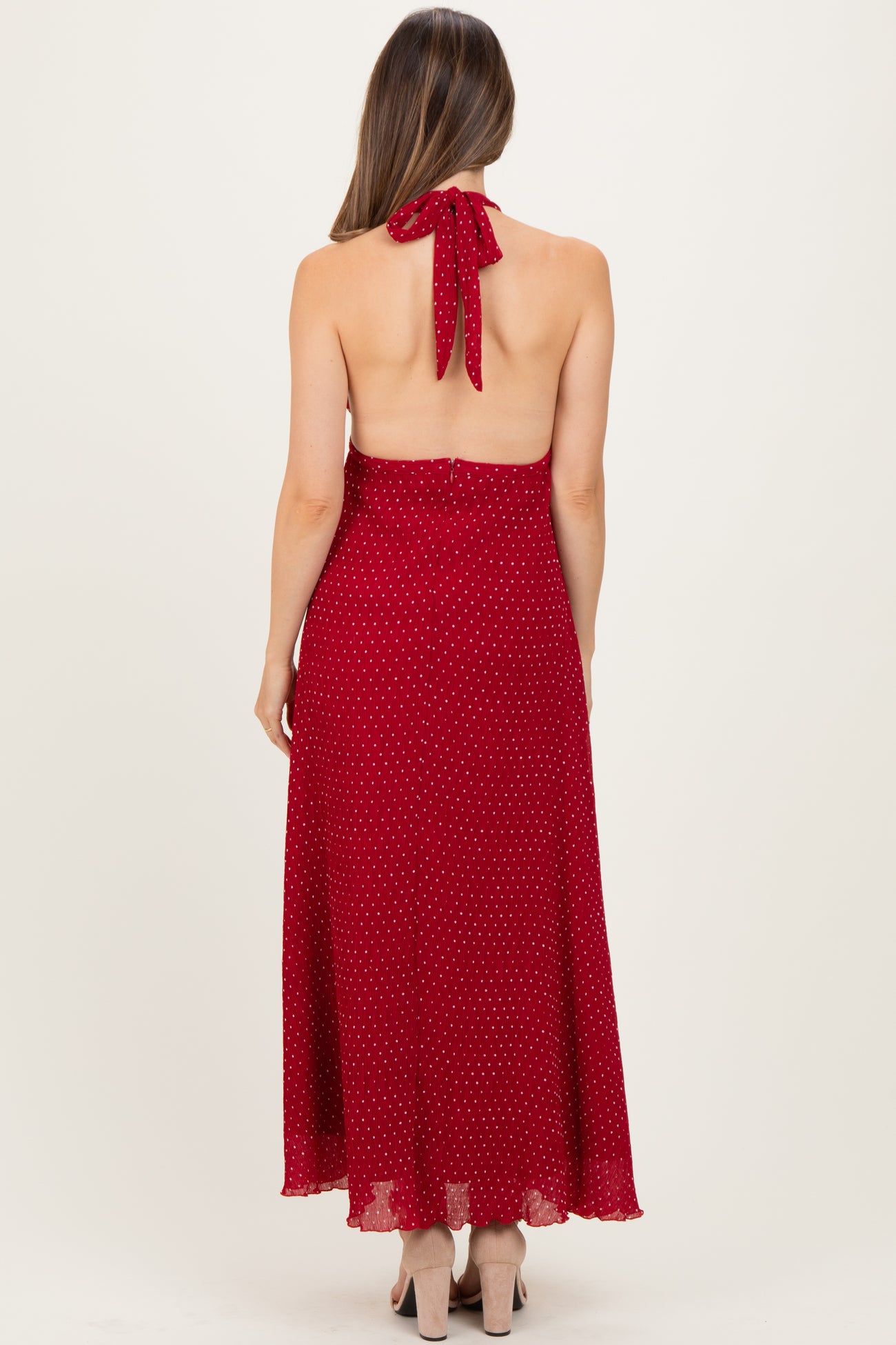 woman wearing a red polka dot maternity maxi dress with a halter neck and open back design