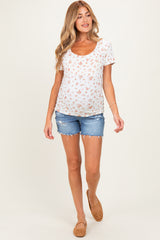 woman wearing a white floral maternity top and denim shorts, showing her baby bump while walking