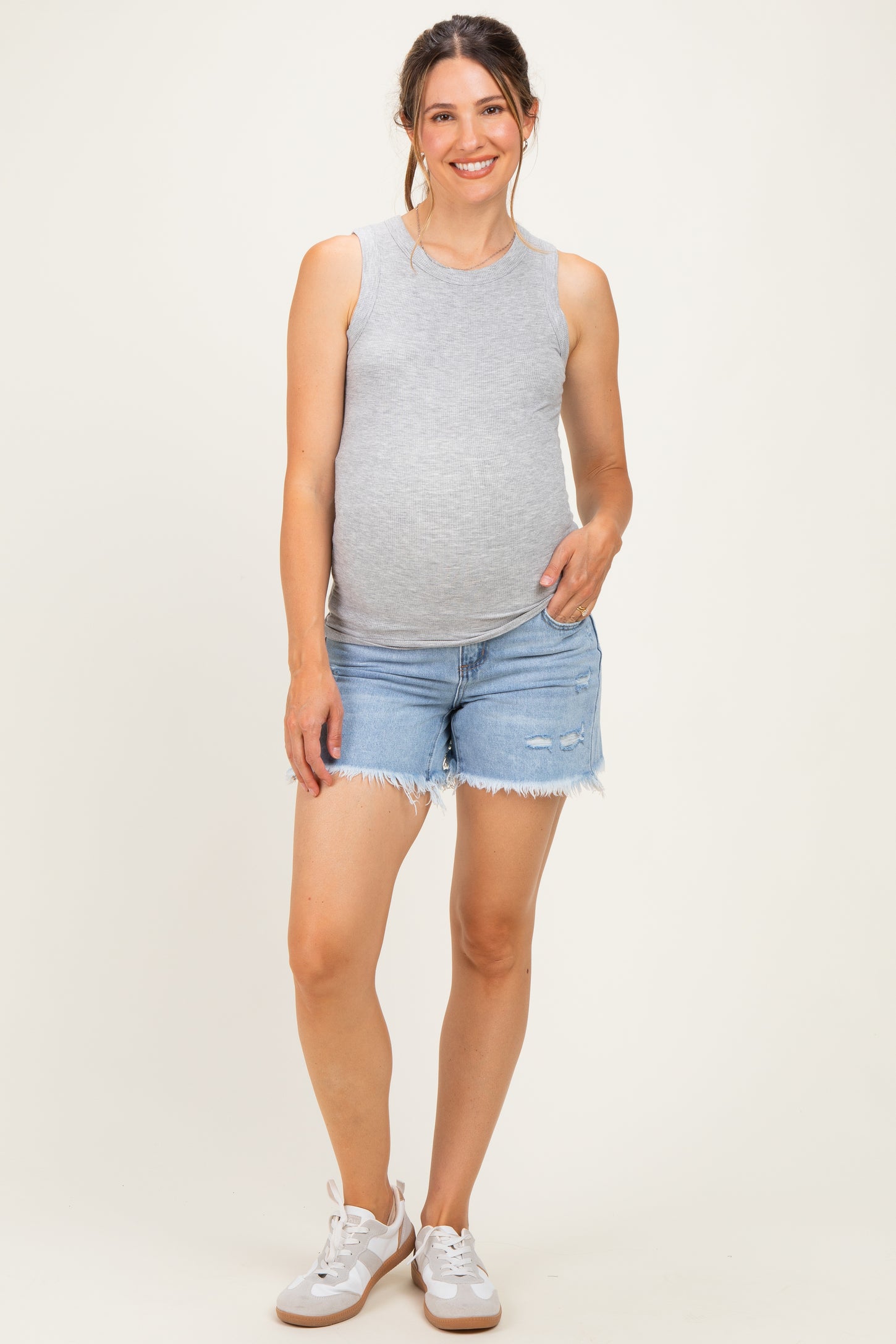 woman wearing a gray sleeveless maternity top and denim shorts, showcasing her baby bump
