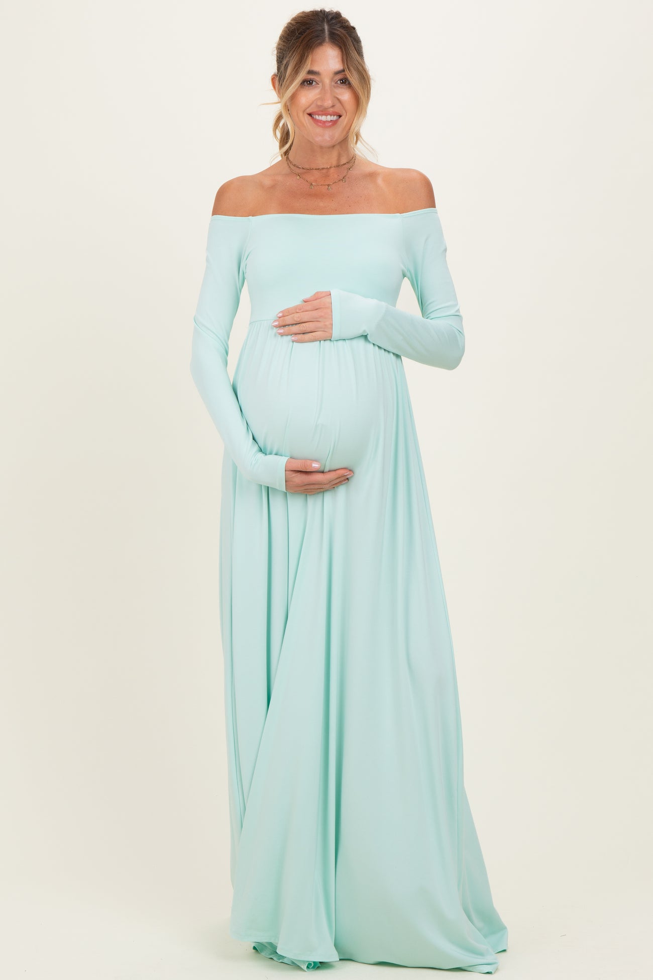 woman wearing a light mint off-shoulder maternity gown and holding her baby bump