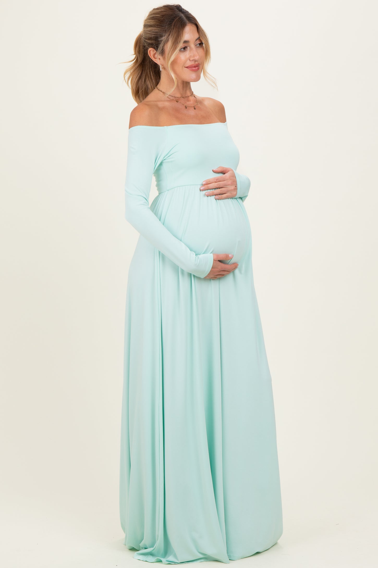 woman wearing a mint green off-the-shoulder maternity gown showing her baby bump