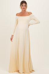 woman wearing a pale yellow off-the-shoulder maternity gown with a flowing skirt and long sleeves, showcasing her baby bump