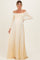 woman wearing a pale yellow off-the-shoulder maternity gown with a flowing skirt and long sleeves, showcasing her baby bump