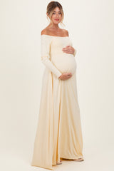 woman wearing a cream off-shoulder maternity gown, showcasing her baby bump, standing gracefully against a neutral background