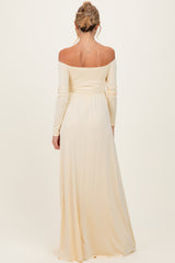 woman wearing a light beige off-the-shoulder maternity gown with long sleeves, showing a flowing silhouette from the back