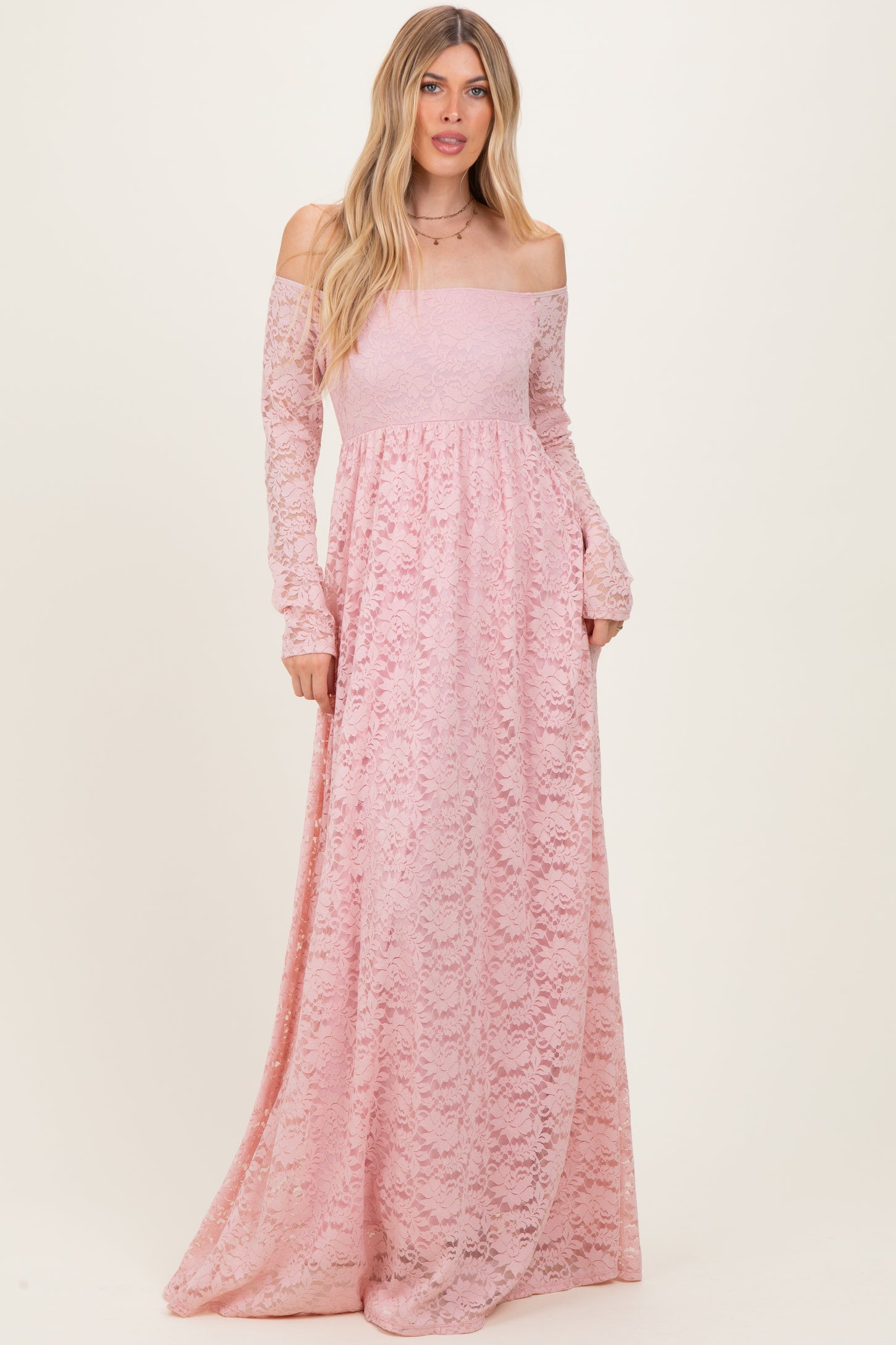 woman wearing a long pink lace off-shoulder maxi dress with long sleeves and a flowing silhouette