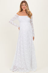 woman wearing a white lace off-shoulder maternity dress with long sleeves and a flowing skirt, showcasing her baby bump