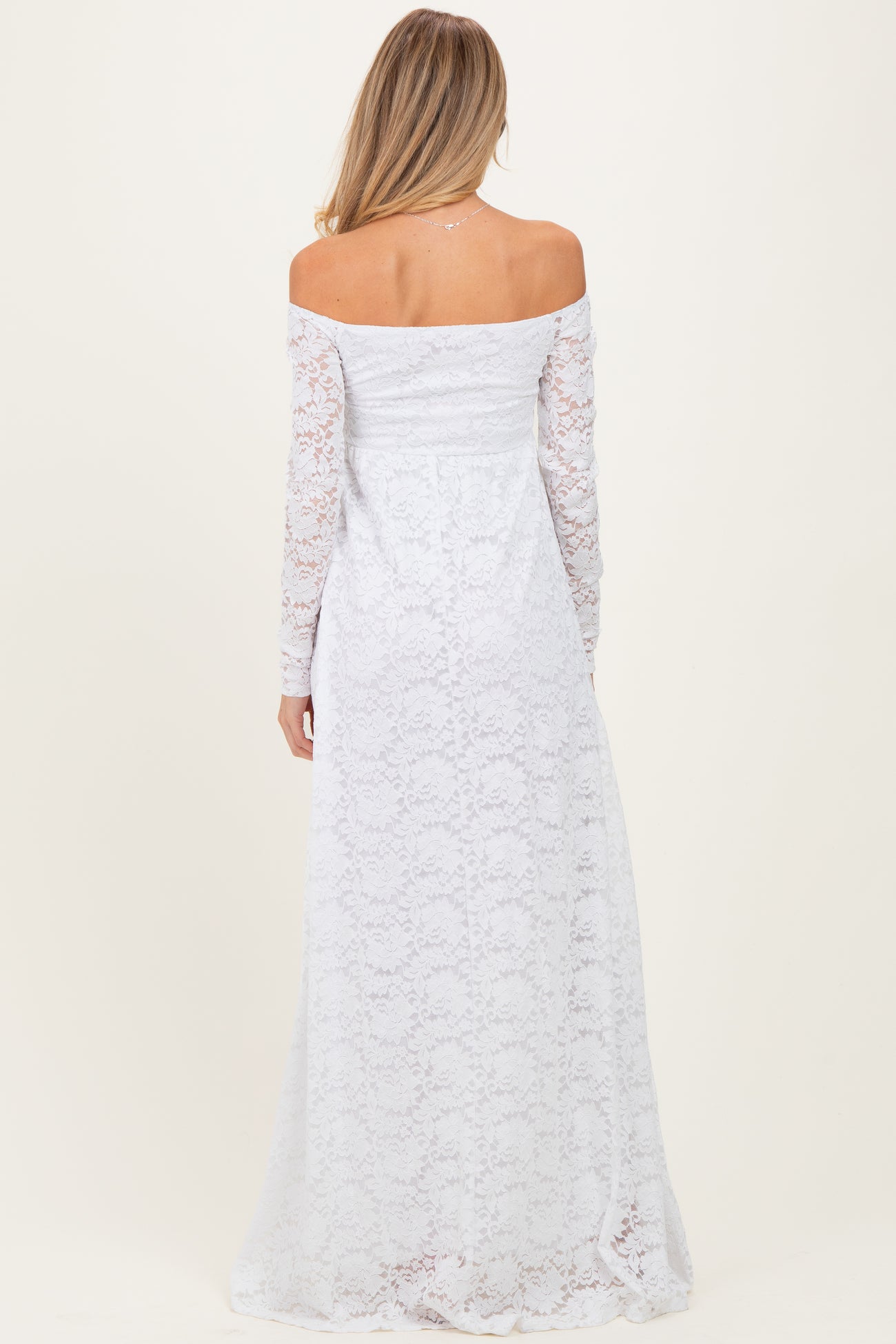 woman wearing a white off-the-shoulder lace maternity dress with long sleeves, showing a flowing skirt from the back