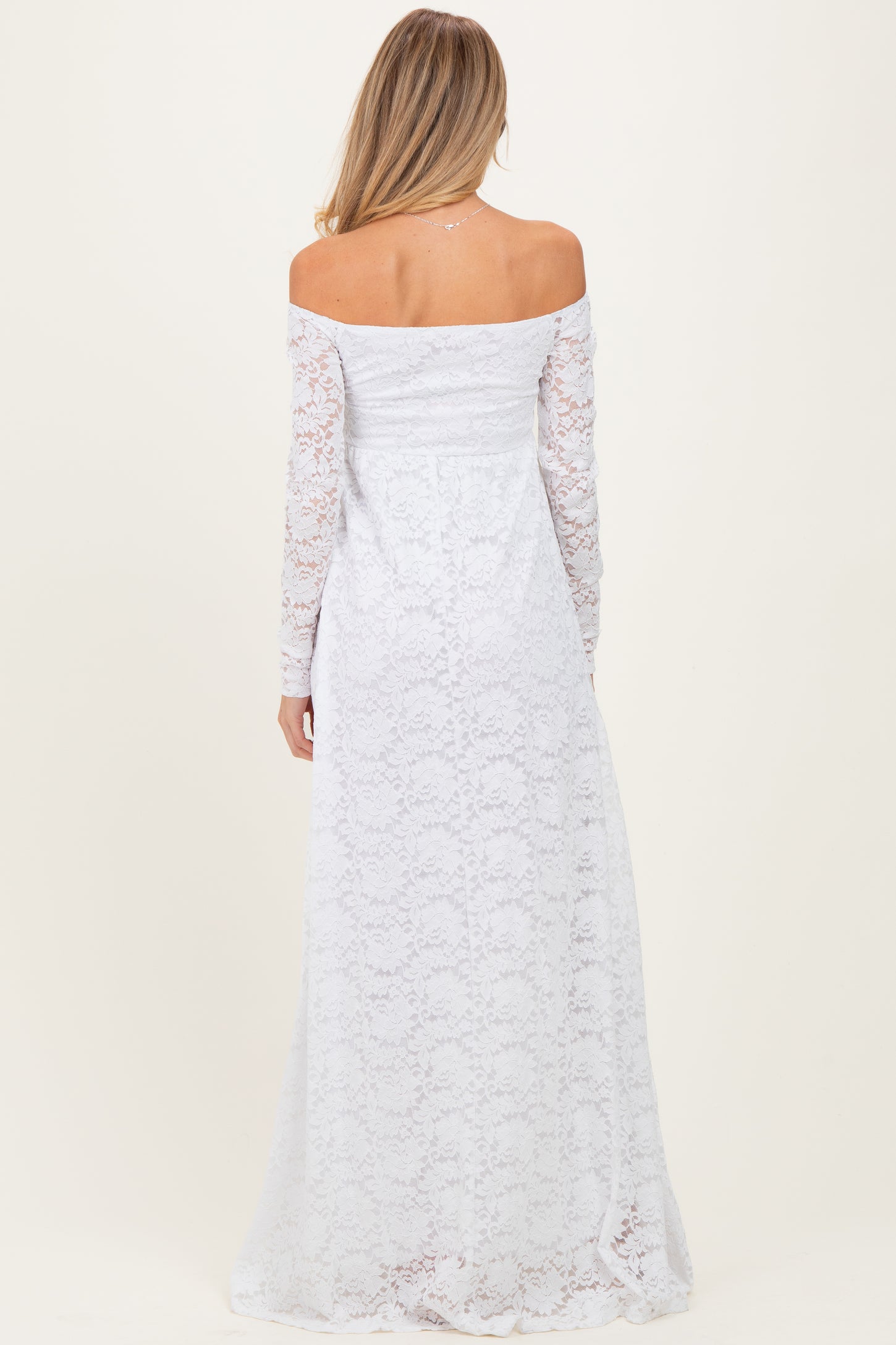 woman wearing a white off-the-shoulder lace maternity dress with long sleeves, showing a flowing skirt from the back