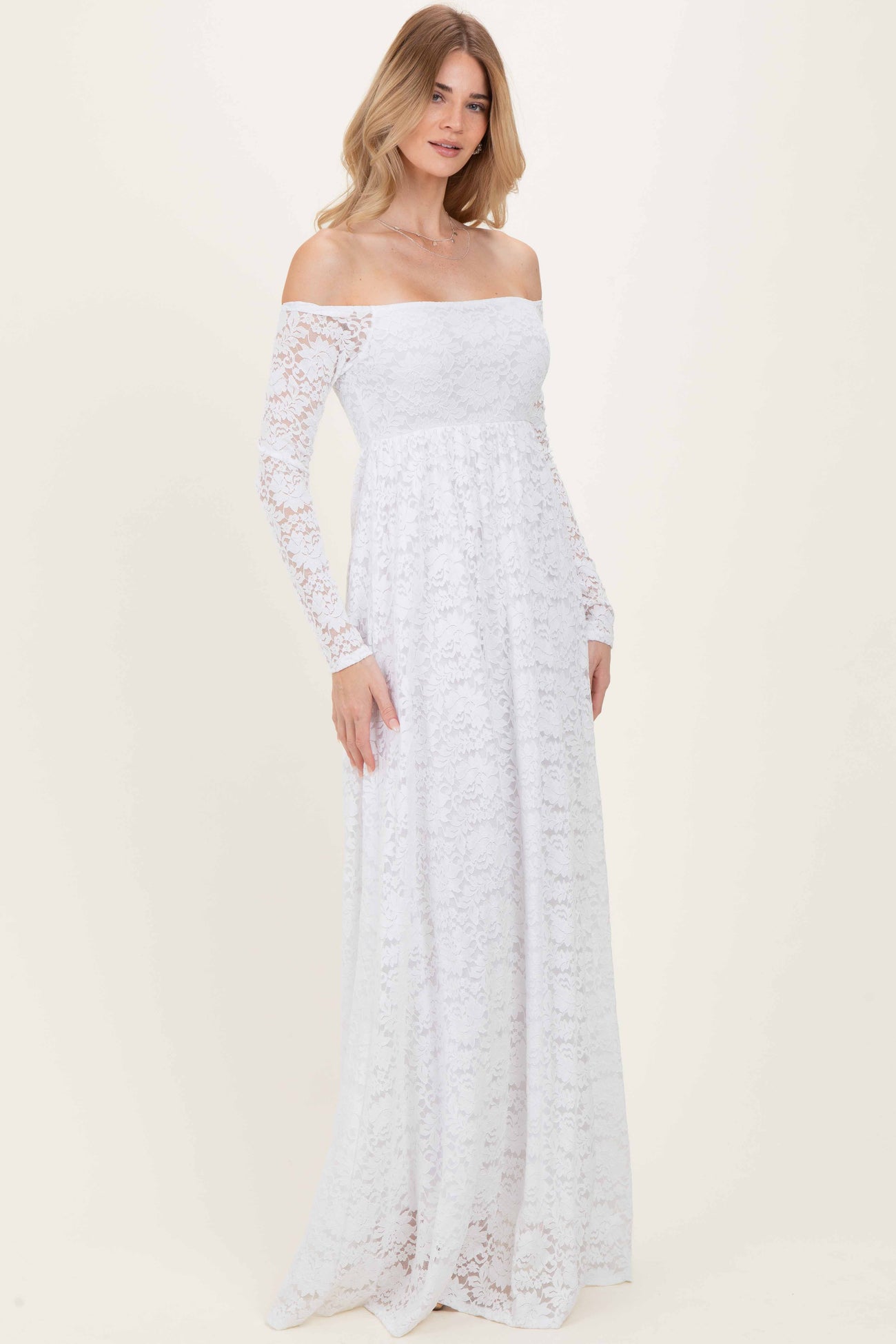 woman wearing a white off-the-shoulder lace maxi dress with long sleeves and a flowy skirt