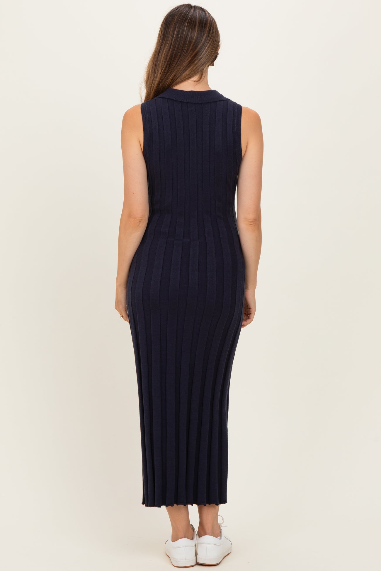 woman wearing a navy blue ribbed sleeveless maternity dress, showing a fitted silhouette and ankle-length design