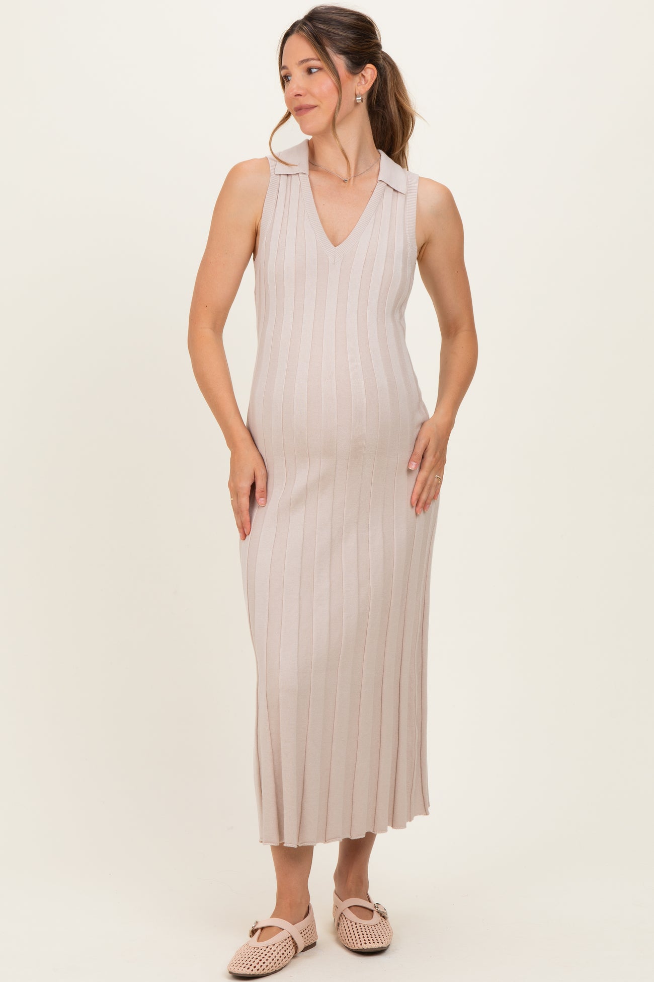 woman wearing a light beige maternity dress with a v-neck and vertical stripes, holding her baby bump