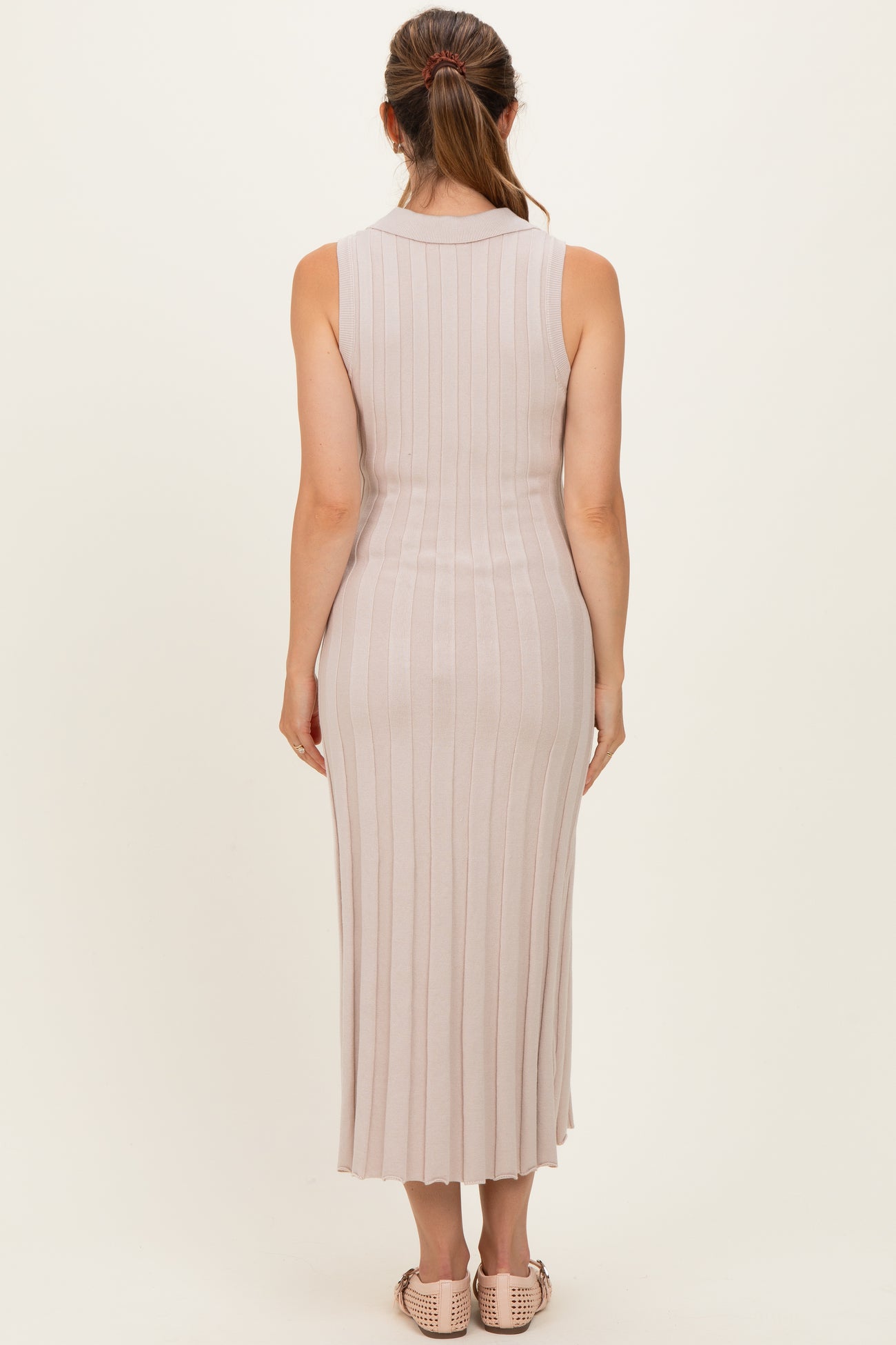 woman wearing a fitted light pink ribbed maternity dress with a midi length and sleeveless design, showing her back