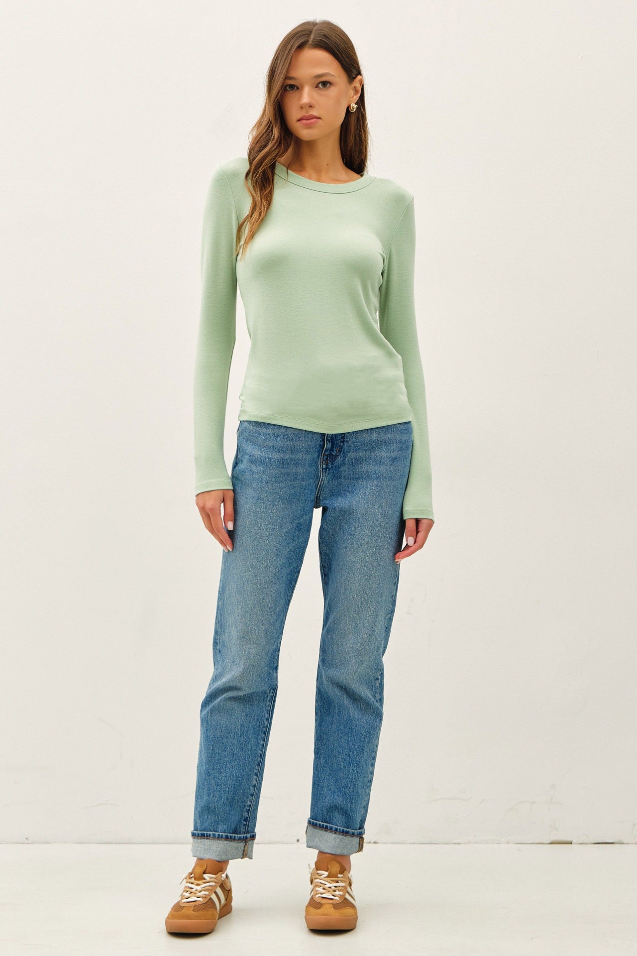 woman wearing a light green long sleeve top and blue straight leg jeans with casual sneakers