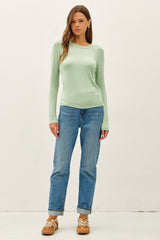 woman wearing a light green long sleeve top and blue straight leg jeans with casual sneakers