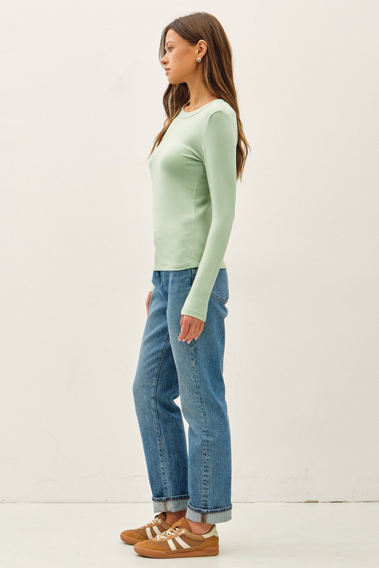 woman wearing a light green long sleeve top and blue high-waisted jeans, standing sideways
