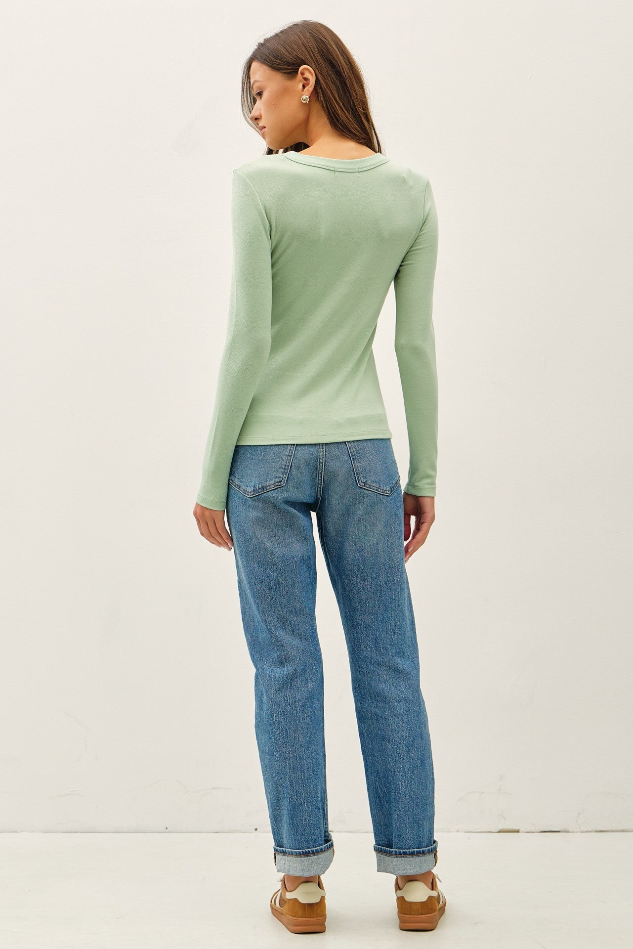 woman wearing a light green long sleeve top and blue high-waisted jeans, seen from the back
